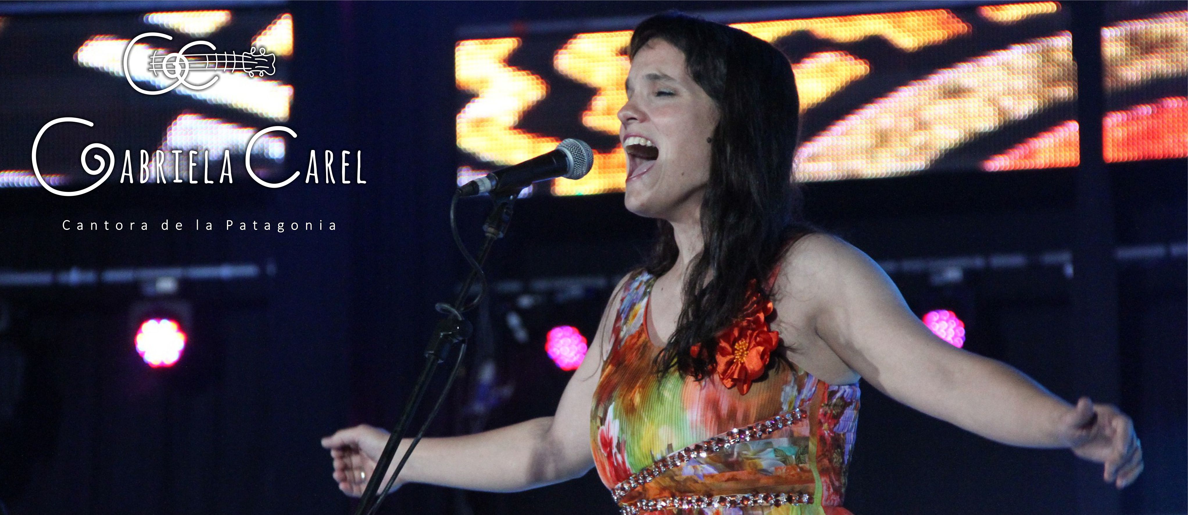 Gabriela Carel cantando en Cosquín. Actitud abriendo los brazos, con un vestido floreado color naranja