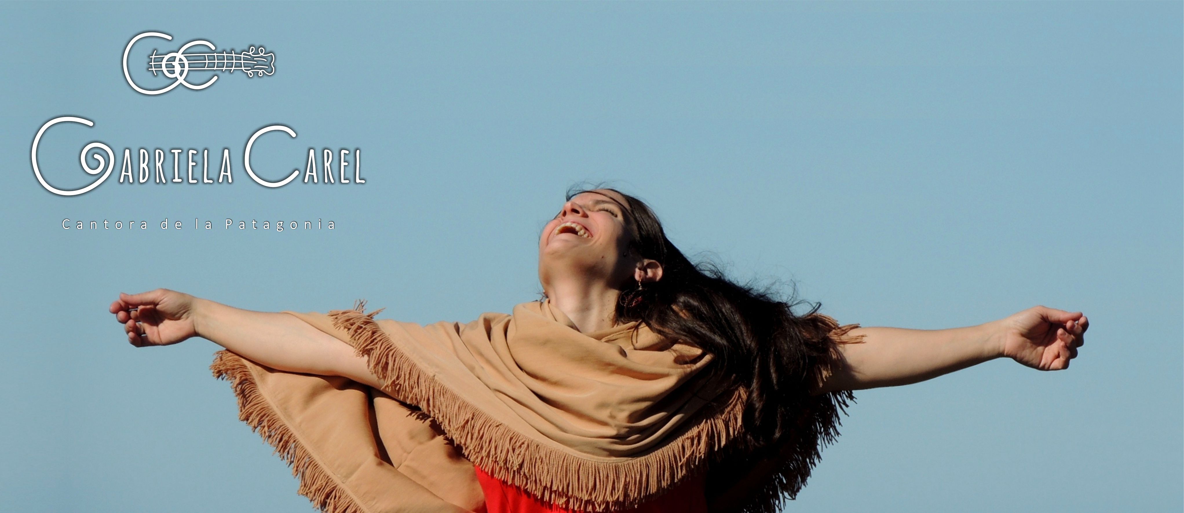 Gabriela Carel en actitud de brazos abiertos y rostro hacia el cielo. De fondo un cielo pleno, celeste. Durante filmación del videoclip Loncomeo con aire de aquí